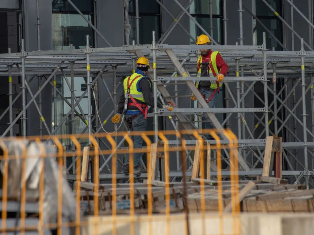 Dos trabajadores de la construcción con casco y equipo de seguridad sobre un andamio